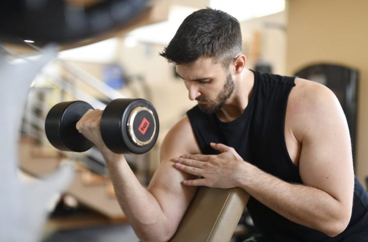 forearm exercises,''A muscular man sitting down and focused on performing a dumbbell curl, showcasing his forearm and bicep definition.