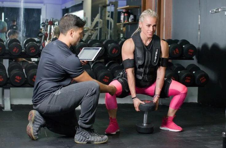 A fitness coach assisting a woman with her form during an exercise session in a gym.