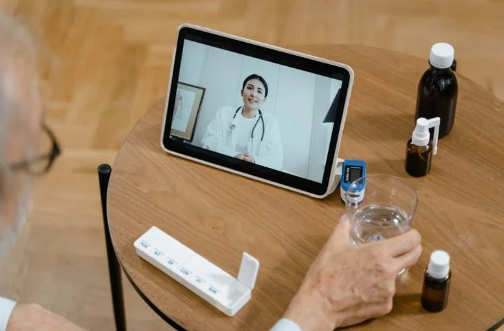 medical-news-today-review-feature-image Medical News Today Review,''A health professional in a white coat appearing on a tablet screen, placed on a wooden desk next to small medical bottles and a glass of water.